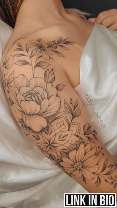 a woman laying on top of a bed covered in white sheets with flowers tattooed on her arm