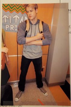 a young man is standing in front of a refrigerator with his arms crossed and looking at the camera