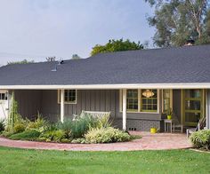 a small house with a large front yard and landscaping around the porch area is shown on a sunny day