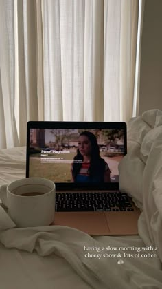 a laptop computer sitting on top of a bed with a cup of coffee in front of it