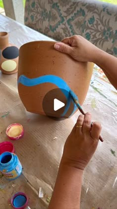 a person is painting a pot with blue paint on the table next to other pots