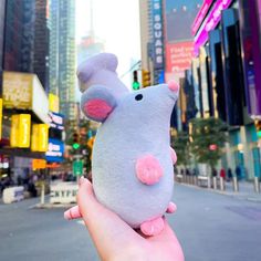 a hand holding a small stuffed animal in the middle of a street with tall buildings