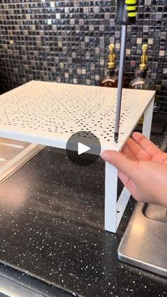 a hand is pointing at the bottom of a white shelf on top of a stove