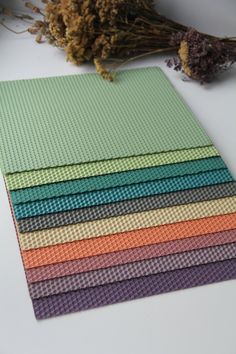 a stack of different colored mats sitting on top of a white table next to dried flowers