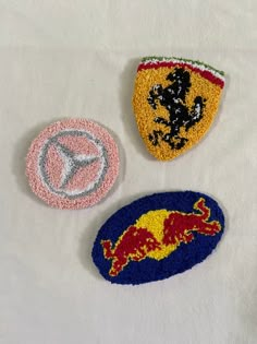 three patches with different designs on them sitting on a white cloth covered tablecloth,