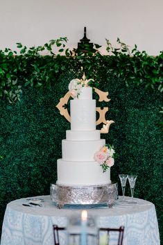 a white wedding cake sitting on top of a table next to a green plant wall