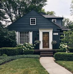 a black house with white trim and flowers on the front door is surrounded by greenery