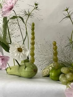 flowers and fruit are arranged on a white table cloth, with long stems in the background