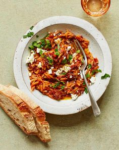 a white plate topped with pasta next to a piece of bread