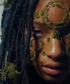 a woman with dreadlocks and green leaves on her face is staring at the camera