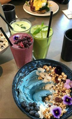 there are many drinks on the table with blueberries and granola in front of them