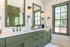 a large bathroom with two sinks, mirrors and green cabinetry on the side wall