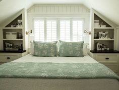 a bed sitting under a window in a bedroom next to a bookcase filled with books