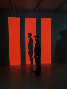 a man standing in front of an orange and black wall with three vertical lines on it