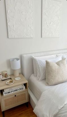 two paintings hang on the wall above a bed with white linens and pillows,