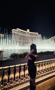 a woman standing in front of a fountain at night with her hand on her face