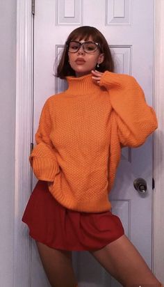 a woman in an orange sweater and red skirt poses for the camera with her hands on her hips