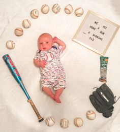 a baby laying on top of a white blanket next to baseballs and a bat