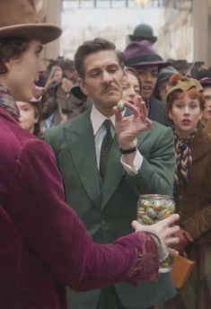 a man in a green suit and tie is talking to another man wearing a hat