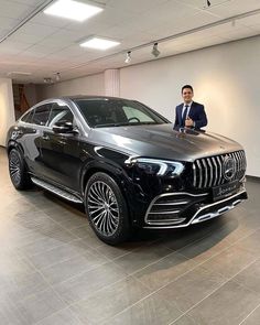 a man standing next to a black mercedes suv in a showroom with white walls