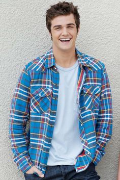 a smiling young man standing in front of a white wall