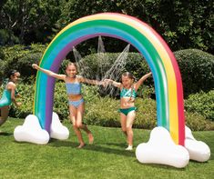 two girls in bathing suits are running under an inflatable rainbow arch