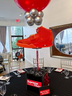 a pair of red sneakers on top of a black table with silver balloons in the background