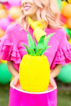 a woman in a pink dress holding a yellow pineapple