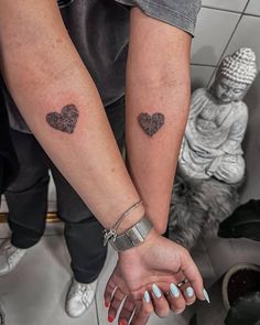 two people holding hands with small tattoos on their arms and one has a heart in the middle