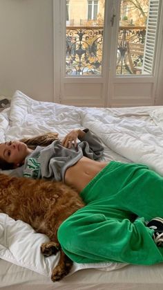 a woman laying on top of a bed next to a large brown dog in a green shirt