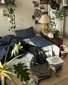 an unmade bed in a bedroom with plants on the wall and pictures hanging above it