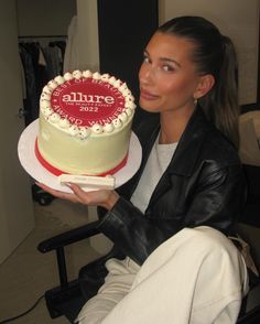 a woman sitting in front of a cake on top of a white plate with red lettering