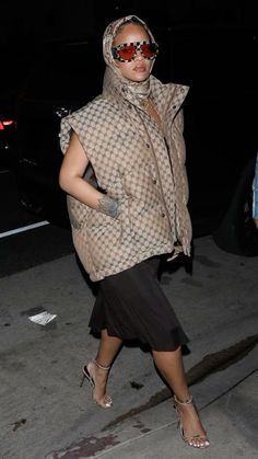 a woman walking down the street at night wearing sunglasses and a scarf over her head