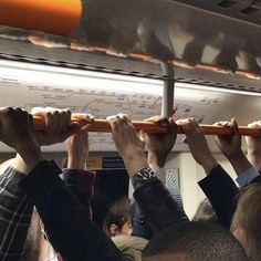 many people are holding up their hands on the subway train, while one person holds an orange object above his head