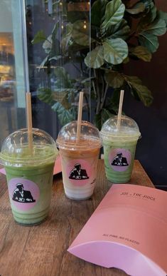 three iced drinks sitting on top of a wooden table next to a pink menu paper