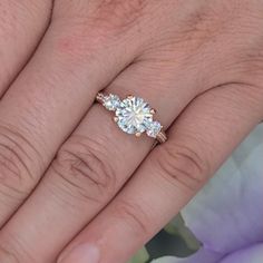 a woman's engagement ring with three stones on her finger and the other hand holding it