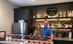 a man and woman standing behind a bar filled with wine glasses