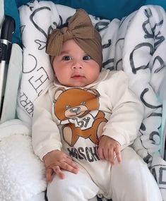 a baby is sitting in a stroller wearing a sweater with a bow on it's head