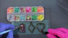 two hands in purple gloves are holding scissors and some colorful beads on a display case