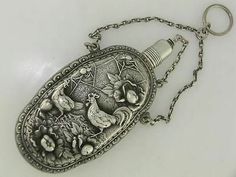 an antique silver bottle with birds and flowers on it's side hanging from a chain