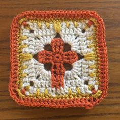 an orange and white crocheted square with a cross on it sitting on a wooden surface