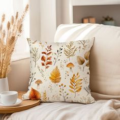 a coffee cup on a tray next to a pillow with autumn leaves printed on it