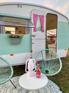 a table and chairs in front of a trailer with pink curtains on the windowsill