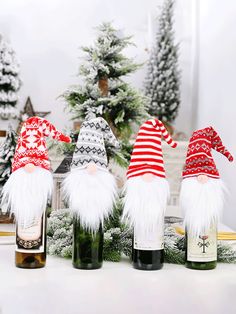 three wine bottles with gnome hats on them sitting next to some christmas decorations and trees