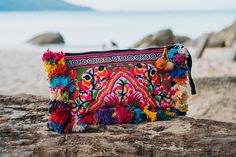 a colorful purse sitting on top of a wooden log near the ocean and rocks in front of it