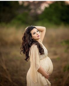 a pregnant woman poses for a photo in a field with her hands behind her head