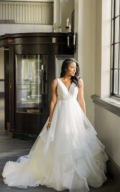 a woman in a white wedding dress is standing by a window and looking off into the distance