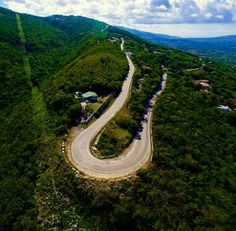 an aerial view of a winding road in the middle of a green mountain side area