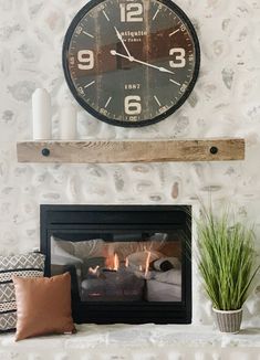 a fireplace with a clock on the wall above it and some plants next to it