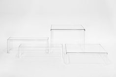 three clear tables sitting side by side on a white surface, one is empty and the other has no legs